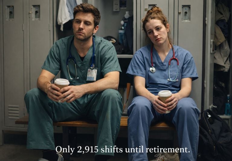 Burned out nurses in blue scrubs holding coffee in a hospital locker room.