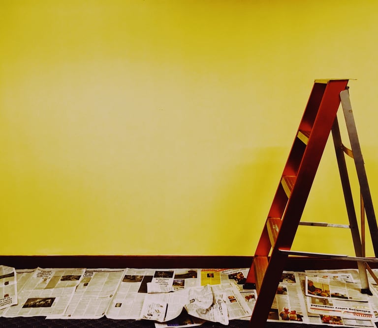 intérieur avec un mur jaune, avec un escabot en bois marron, ave du papier journal au sol 