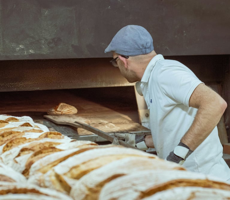 Panadero utilizando una pala de madera para hornear pan de masa madre en un horno tradicional