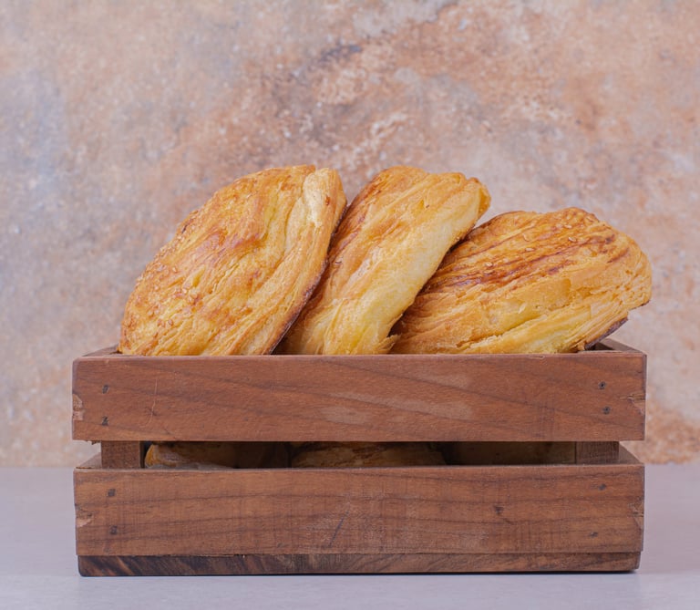 Hojaldres dorados y hojaldrados servidos en una caja rústica de madera sobre un fondo de piedra.