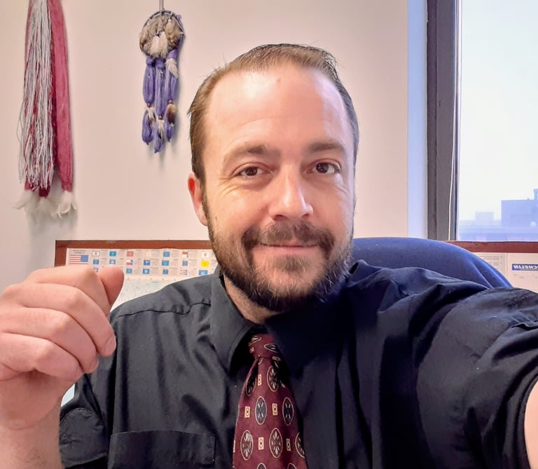 Professional man with a beard wearing a black dress shirt and patterned tie in an office.