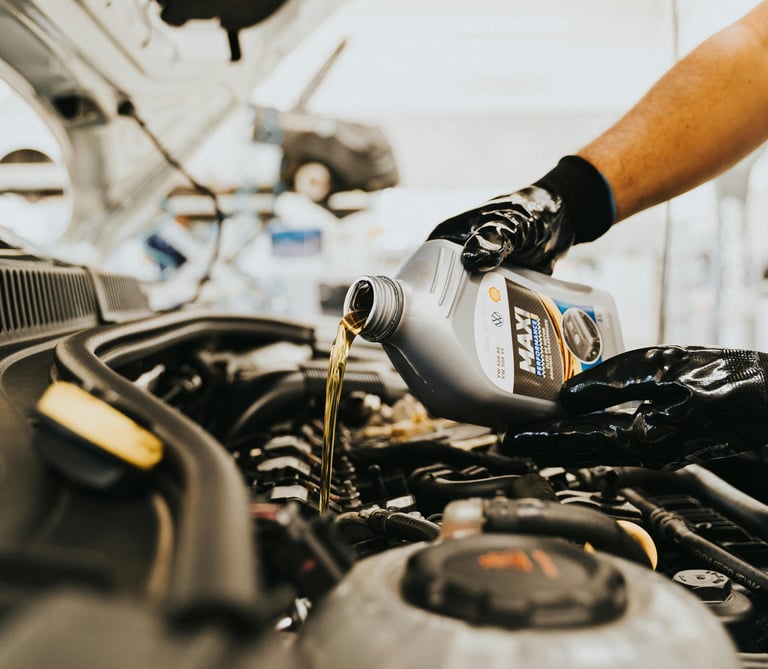 Professional mechanic pouring fresh synthetic engine oil into a car during a routine oil change service.