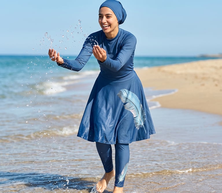 A woman wearing a blue modest burkini swimsuit with a feather print splashes water at the beach.