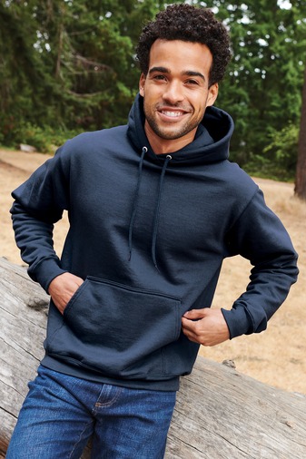 a man in a blue hoodie and jeans standing in front of a log cabin
