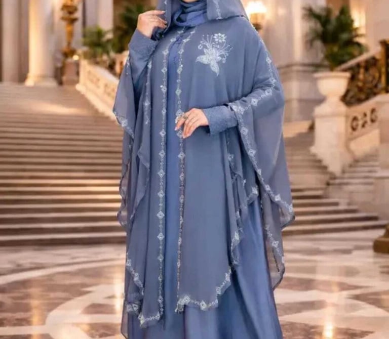 Elegant woman wearing a dusty blue modest abaya dress with floral embroidery and matching hijab.