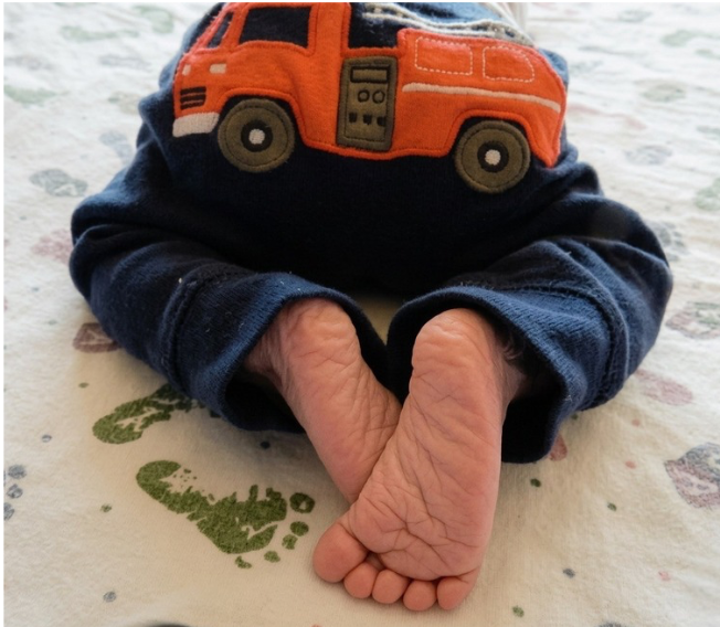 Close-up of a newborn baby's feet wearing navy blue pajamas with an orange fire truck applique.