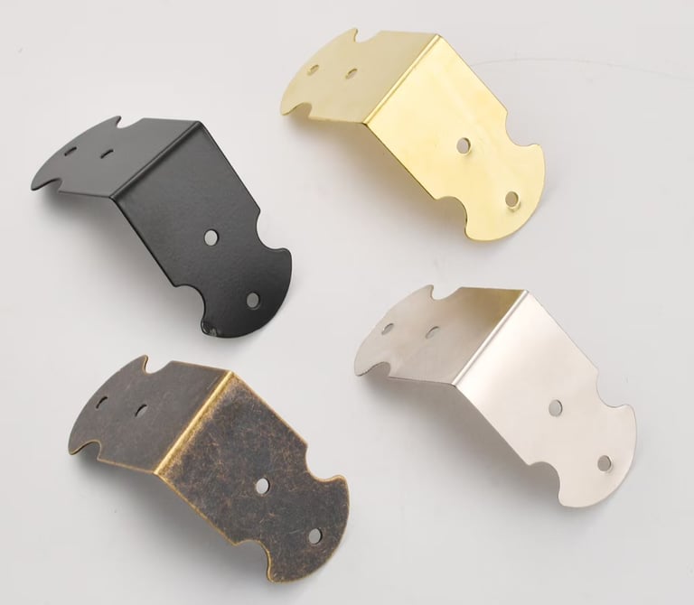 Decorative metal corner protectors in black, brass, silver, and antique bronze finishes for furniture.