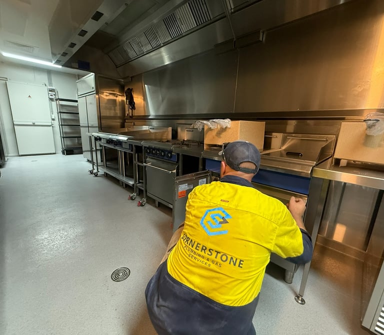 Professional plumber installing commercial kitchen equipment and gas appliances in a restaurant.