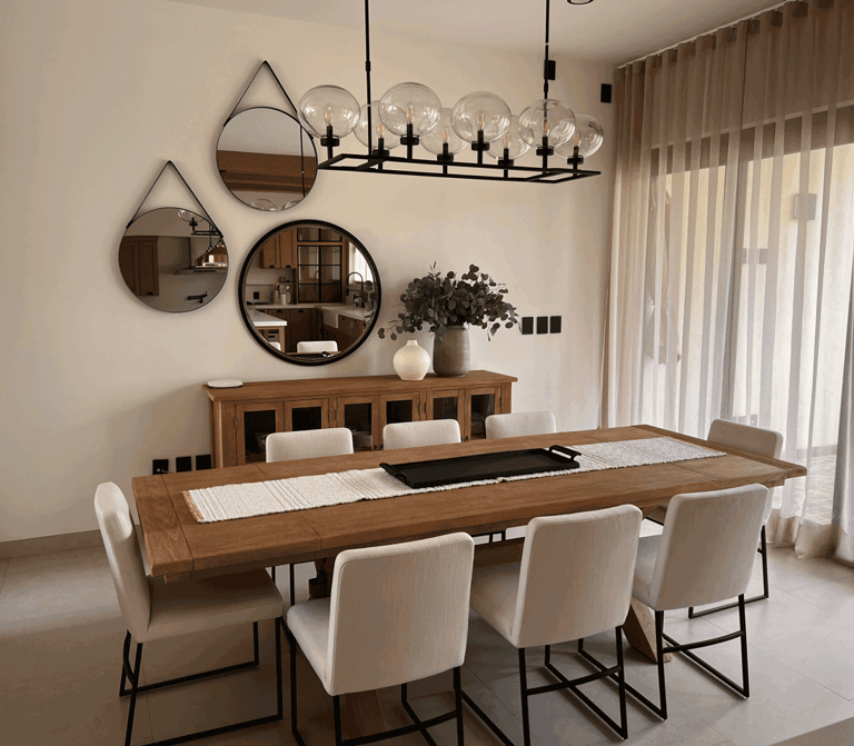 Comedor con mobiliario cálido, espejos decorativos y una lámpara lineal como pieza central | KARÄNA