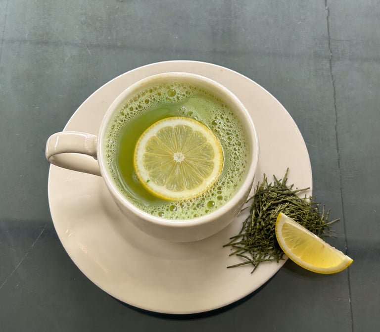 A cup of frothy green matcha tea with a lemon slice garnish and loose tea leaves.