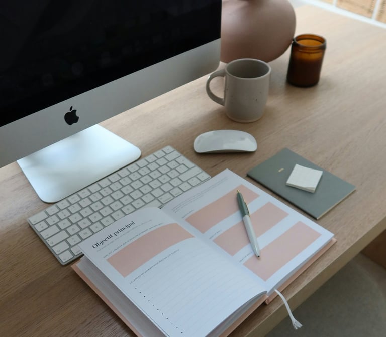 a desktop with an apple computer, coffee and a planner.