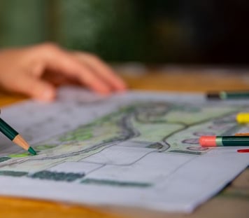 dizainerė laiko pieštuką ir spalvina kraštovaizdžio eskizą