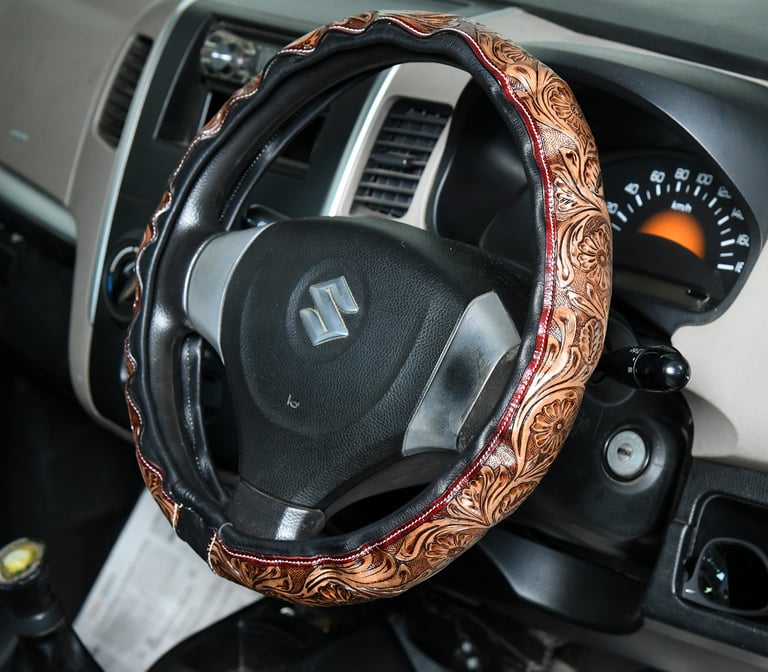 Brown embossed floral leather steering wheel cover on a black Suzuki car interior.