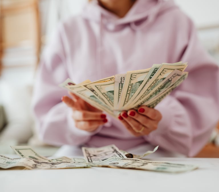 A woman in a pink hoodie, sitting at a tble and counting money.