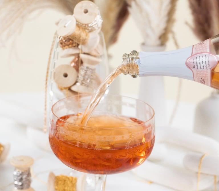a person pouring a drink into a glass of wine with permanent jewelry chains