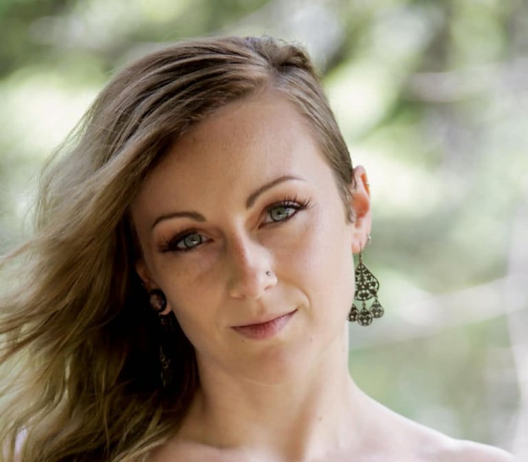 Portrait of a blonde woman with blue eyes wearing ornate bronze chandelier earrings.