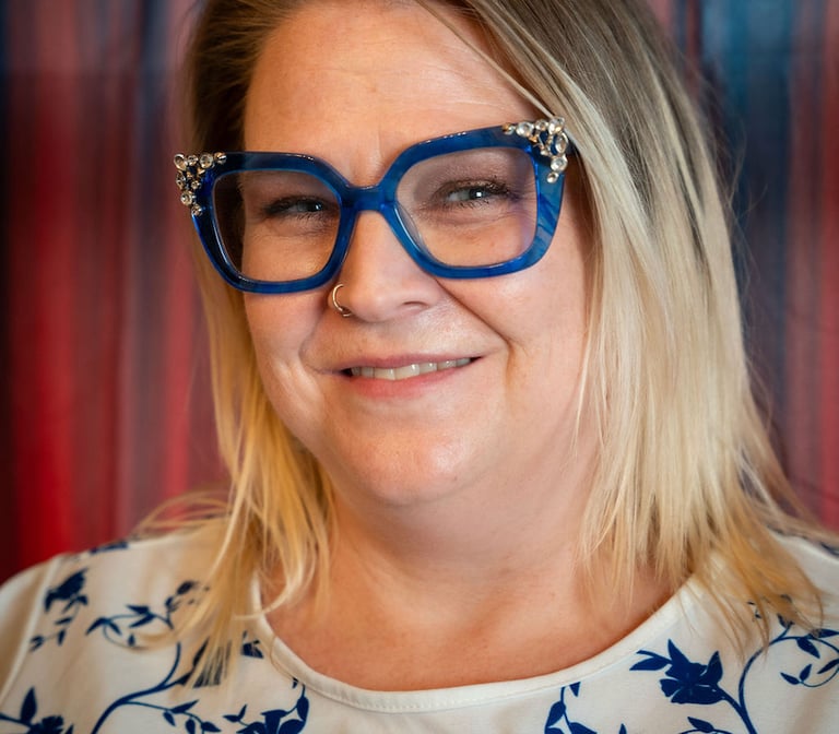 Woman with blonde hair wearing stylish blue floral cat-eye glasses and a white floral blouse.