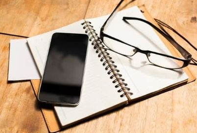 Carnet, lunettes et téléphone illustrant la prise de rendez-vous et les moyens de contact