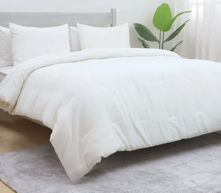 Plush white down alternative comforter set on a bed with matching pillows and a green plant.
