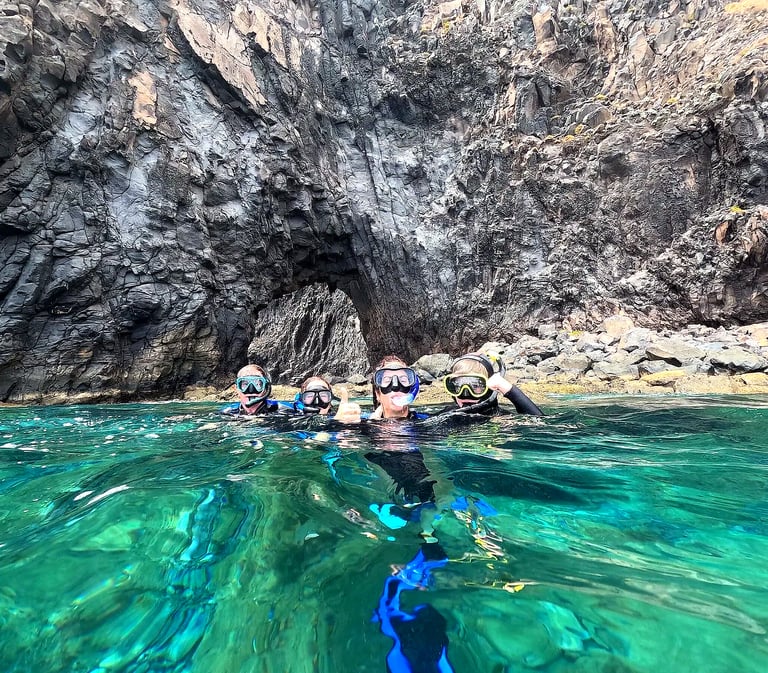 Group of snorkelers in green water in front of a volcanic rock arch at Ponta de São Lourenço, Madeira