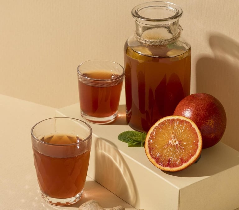 Té de kombucha en una jarra de vidrio, servido con rodajas de naranja  y raíz de jengibre cruda.