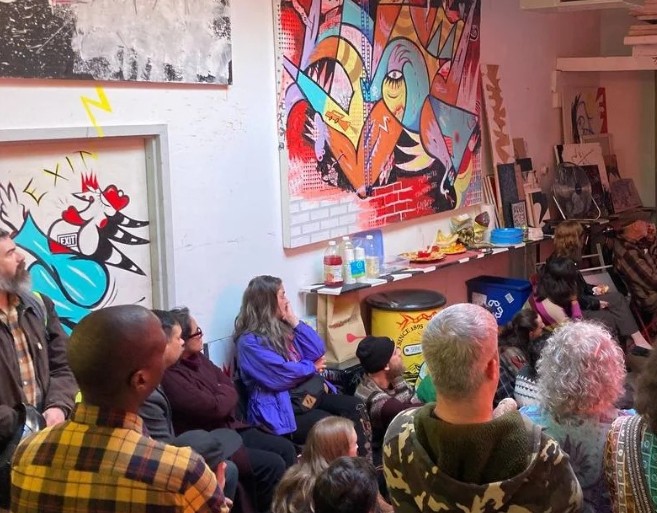 A diverse crowd attends an art gallery exhibition featuring vibrant abstract paintings and street art.