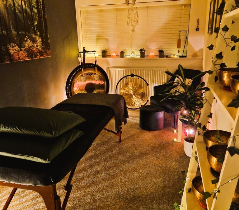 Studio with treatment couch, chair, gongs and shelf with Himalayan singing bowls
