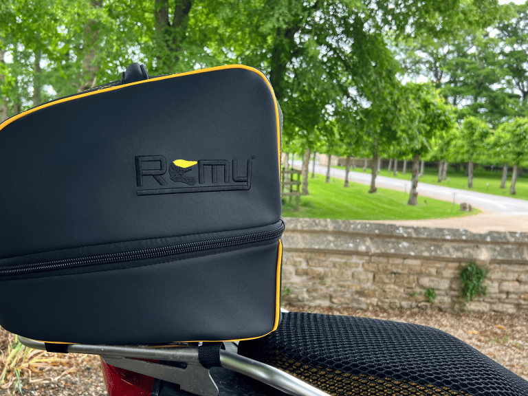 Rider departing on motorcycle with Remy helmet bag secured to the bike, framed against a glowing sun