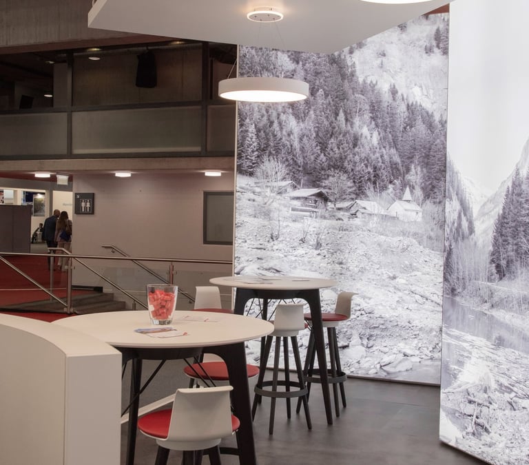 Lounge-Bereich mit Stehtischen und Hockern vor alpiner Bildwelt auf einer Messe.