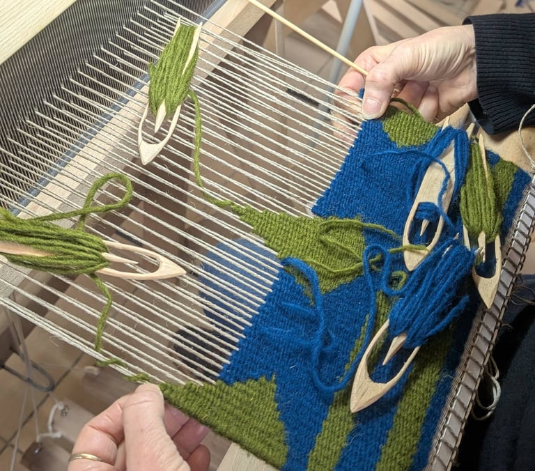 Stagiaire tissant un kilim géométrique en bleu et vert sur un métier à tisser avec navettes