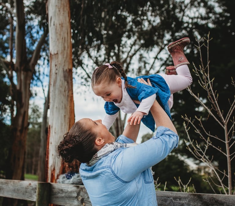 a woman holding a child over her head looking delighted
