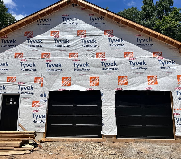 A new garage under construction featuring Tyvek HomeWrap vapor barrier and black garage doors.