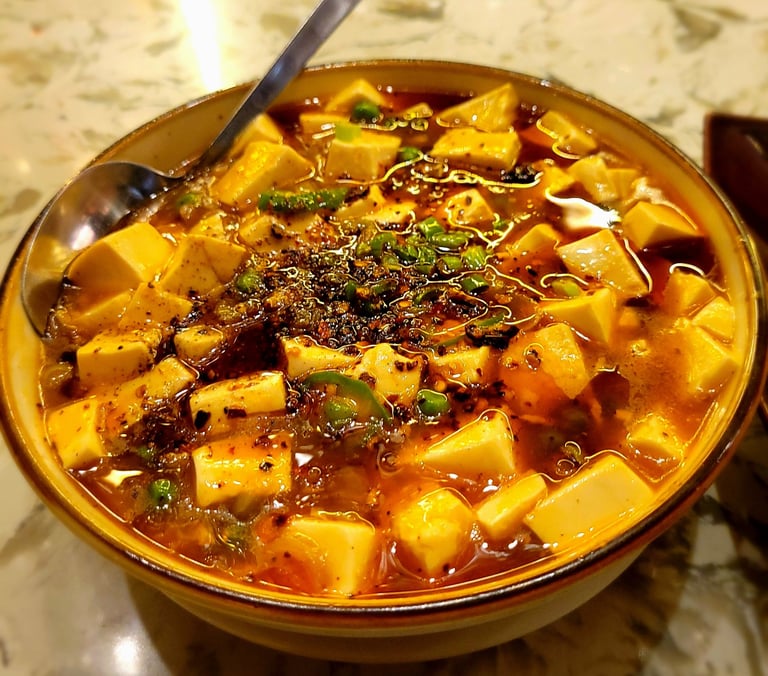 Bowl of Mapo tofu sprinkled with crushed Szechuan peppercorns with floating peas