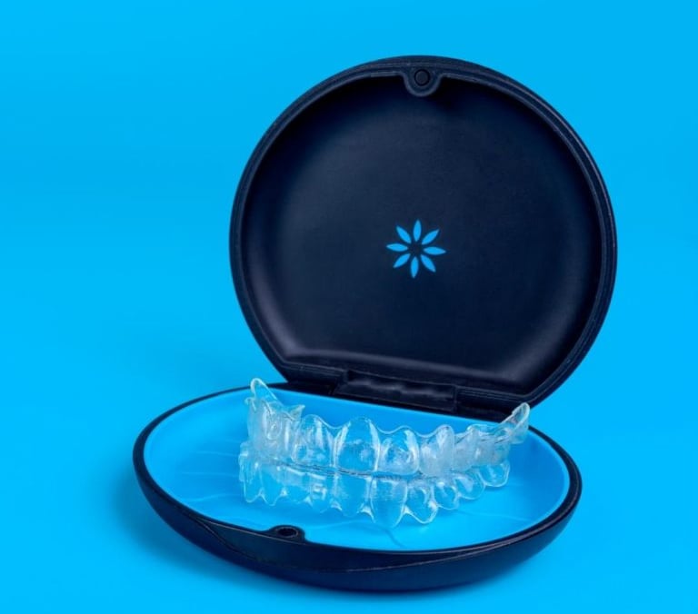 Clear teeth aligners inside a black orthodontic storage case against a bright blue background.