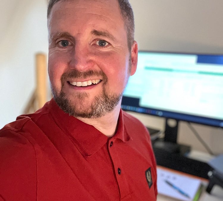 Mike Brown in a red polo shirt working at a home office desk with a computer monitor.