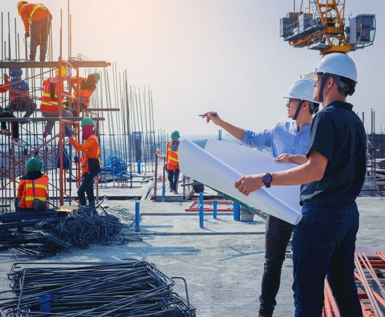 two men in hard hats and safety vests standing in front of a building