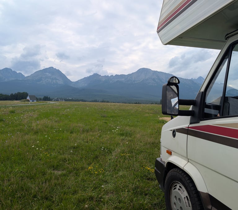 Camper parked on a grassy field with the High Tatras mountains in the background under a cloudy sky