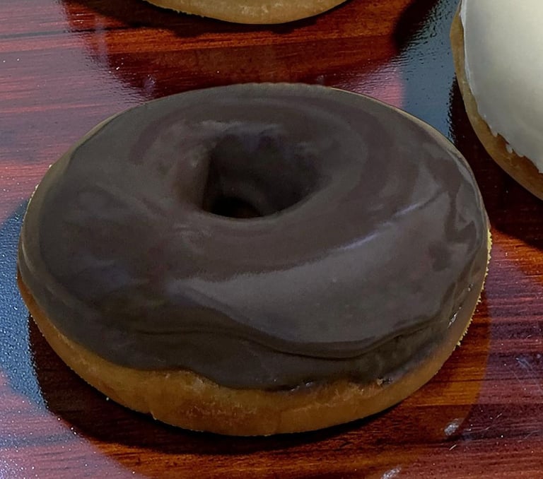 Donut glaseado de chocolate fresco con un suave glaseado oscuro sobre una mesa de madera.