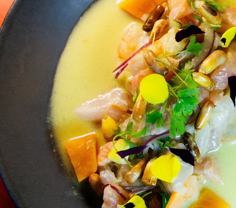 Ceviche Nikkei com peixe branco, camarão, milho crocante, batata-doce e flores comestíveis em um prato fundo escuro