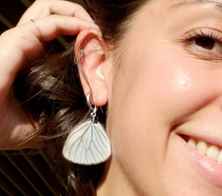 A butterfly earring in a woman's ear. She is smiling.
