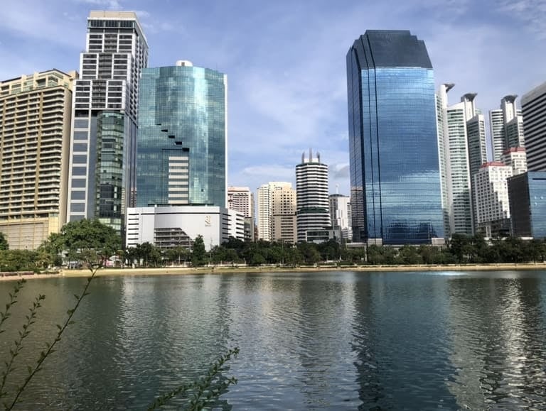 Moderne Wolkenkratzer der Skyline von Bangkok spiegeln sich im ruhigen Wasser des Sees im Benjakitti