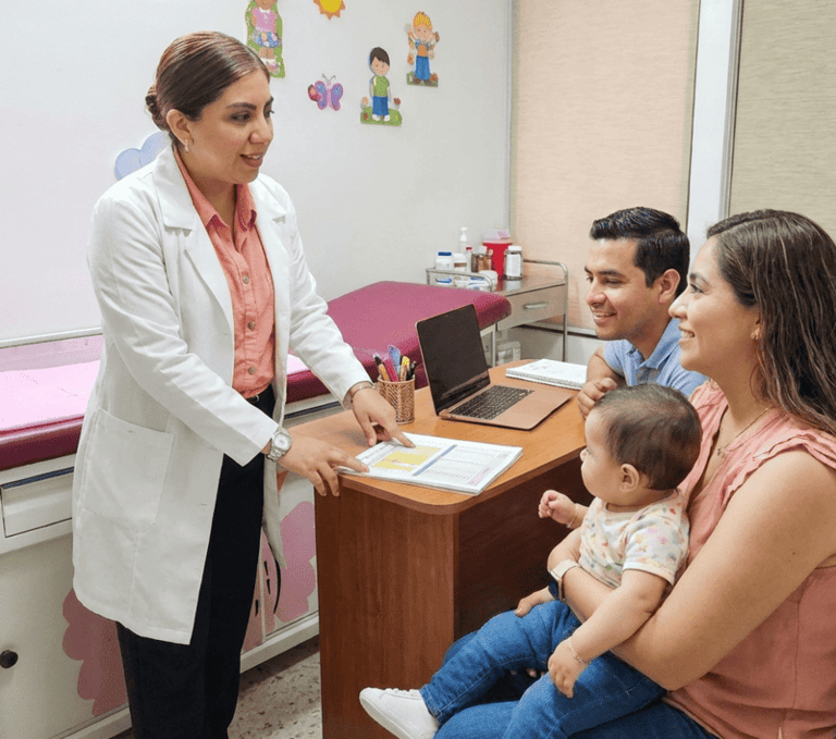 Una pediatra con bata blanca consulta con unos padres y su bebé en una clínica médica.