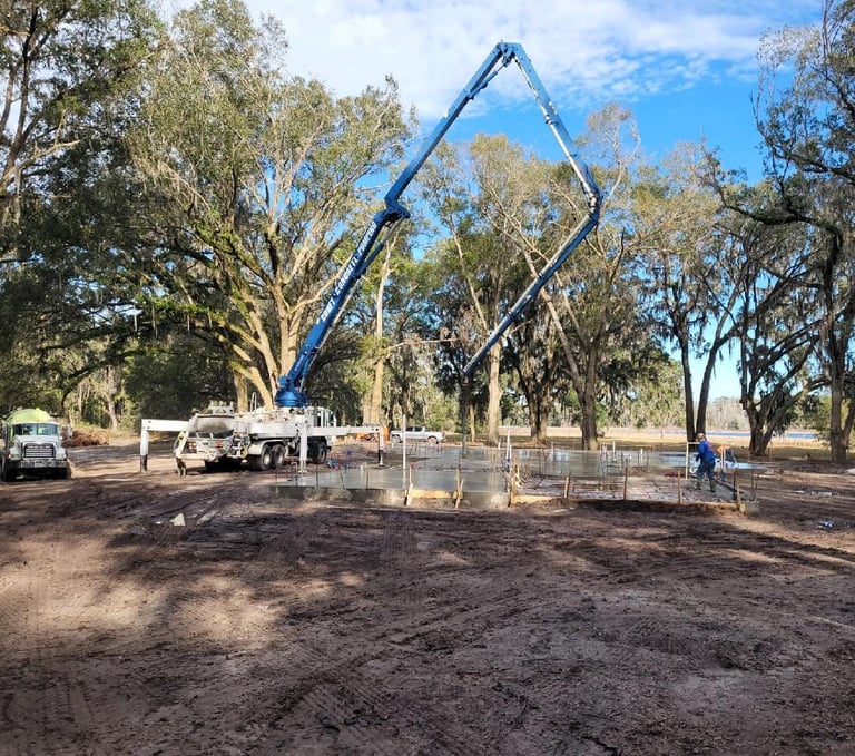 Boom pump pumping comcrete in rural area with trees in background.