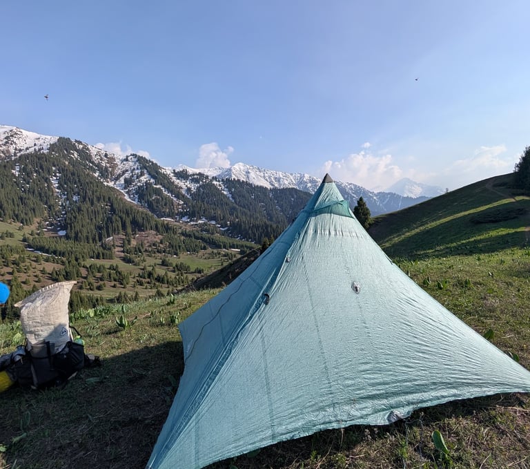 Lightweight Hyperlite Ultamid tent pitched on a grassy mountain ridge overlooking snow-capped peaks.