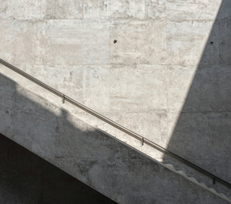An architectural view of a concrete staircase in a modern North American / European museum. The shot is high-angle, emphasizing the repetitive geometry and the play of light and shadow in shades of light gray and white.