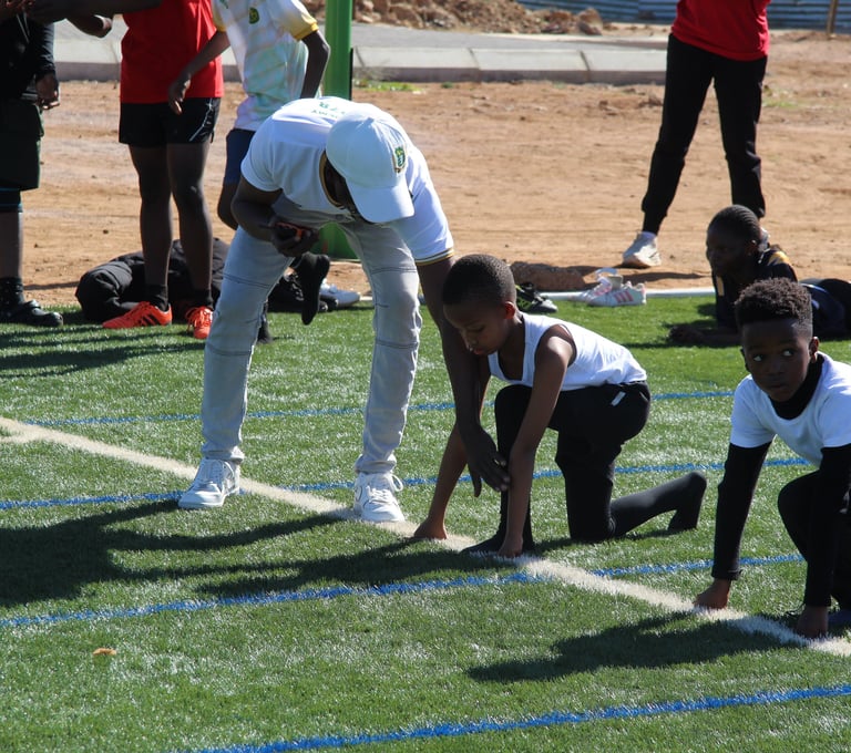 A coach helping young athletes practice their starting position on a green artificial turf running track.