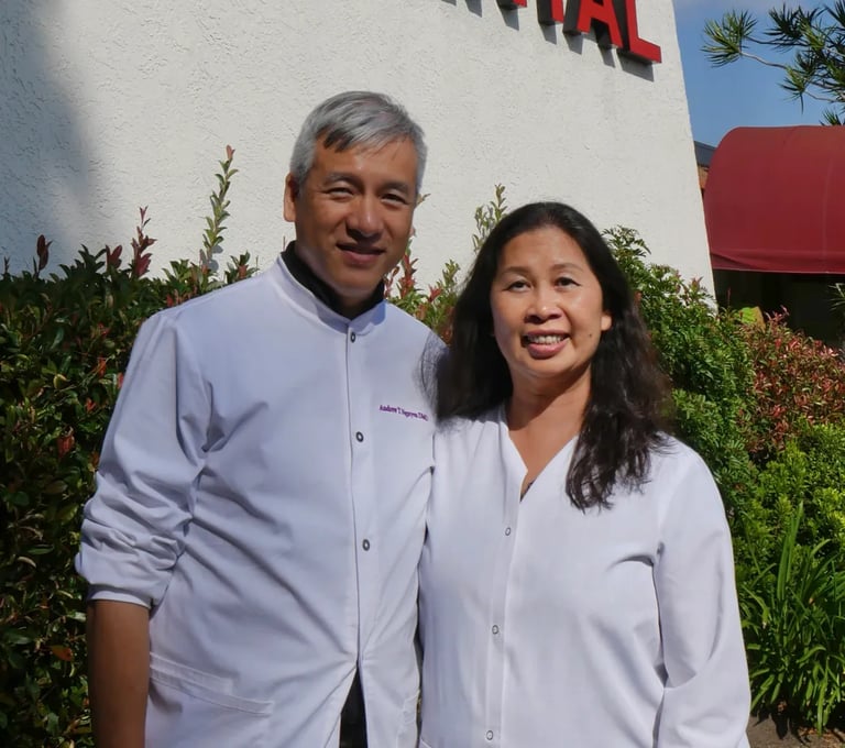 Dr. Andrew Nguyen and female colleague in white dental lab coats standing outside their clinic.