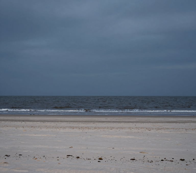 A cinematic photograph of a deserted beach on the North Sea at dusk. The sand is a pale grey-beige, meeting the charcoal tide. Wide, minimalist composition with a vast, heavy sky. Premium storytelling photography.