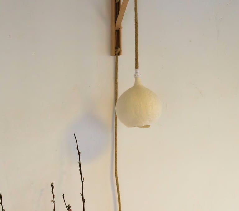Handgemaakte vilten wandlamp Luminosa in maat S, bevestigd aan een houten houder.