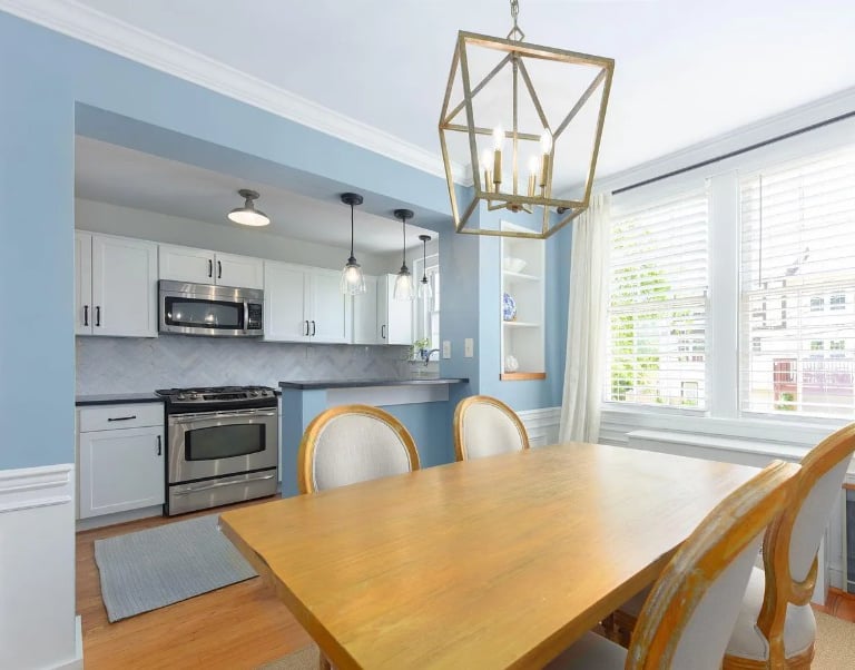 Photograph taken from a dining room looking through a large wall opening into a renovated kitchen